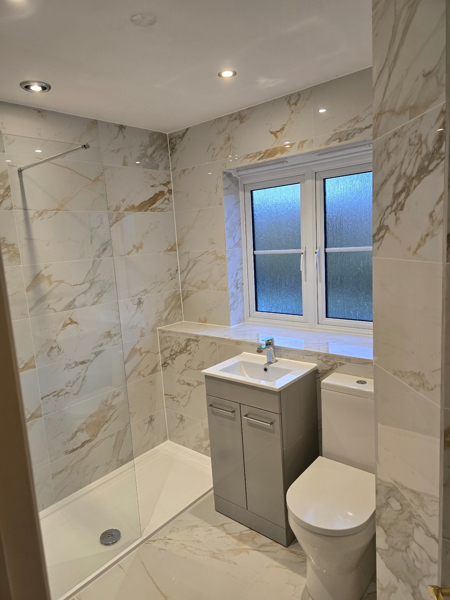 Refurbished marble-effect shower room with grey vanity and WC by Blue Sky