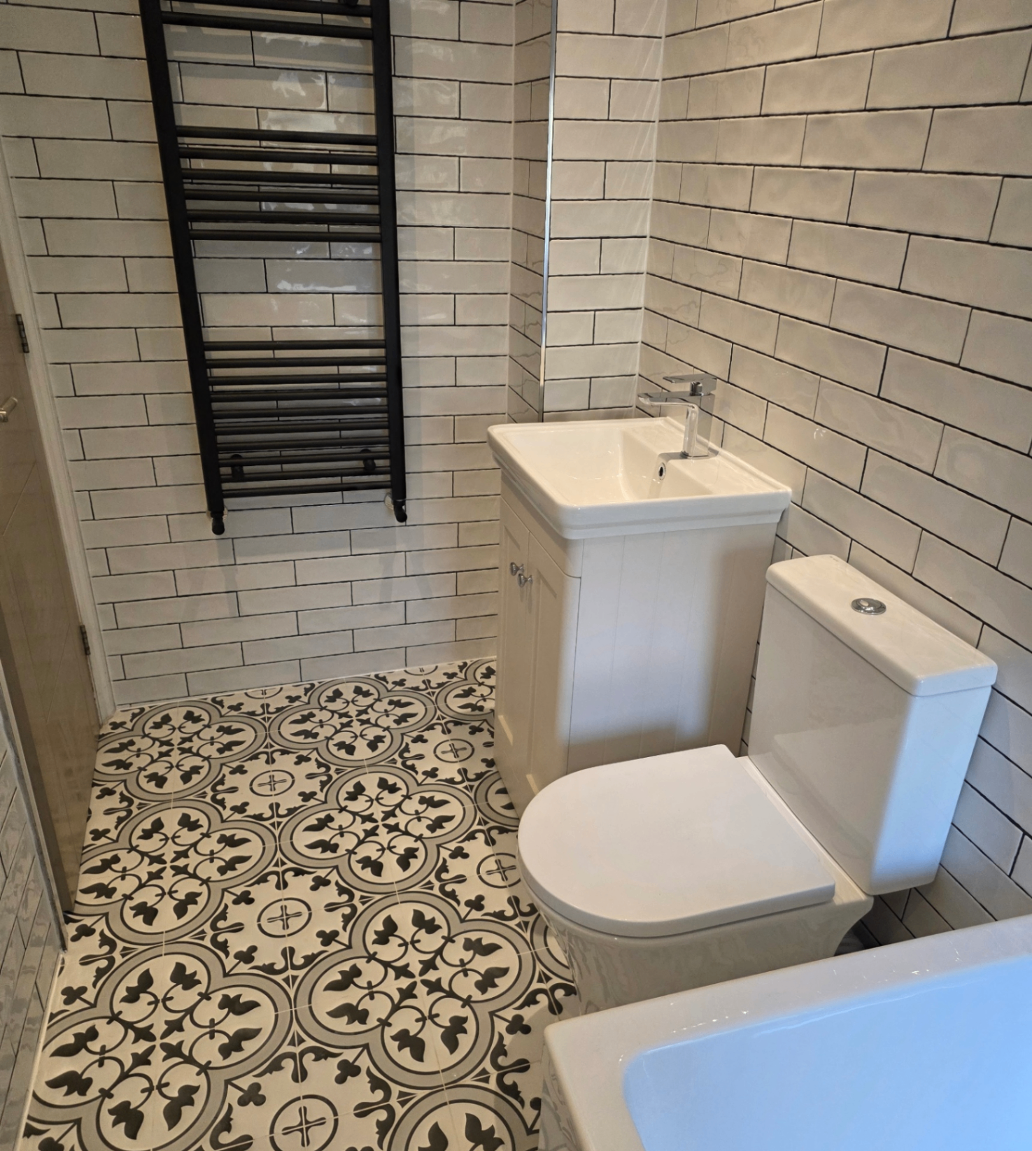 Compact cloakroom with patterned floor tiles, white vanity and black towel rail installed by Blue Sky
