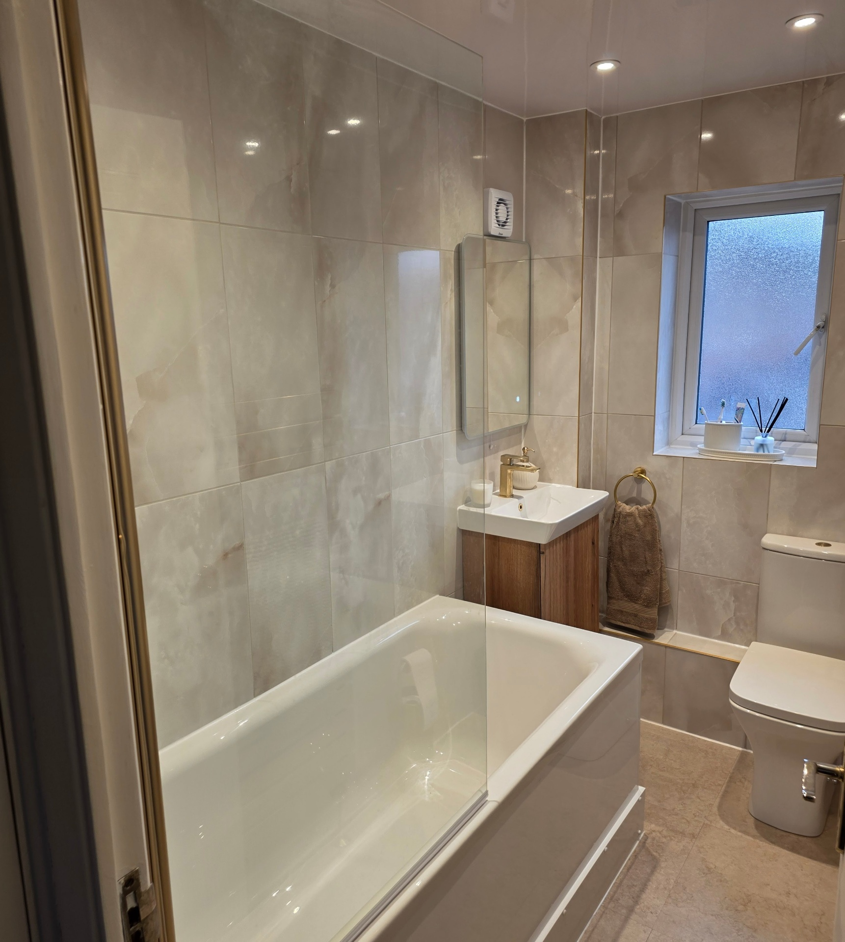 Refurbished beige marble-effect bathroom with bath screen and timber vanity by Blue Sky