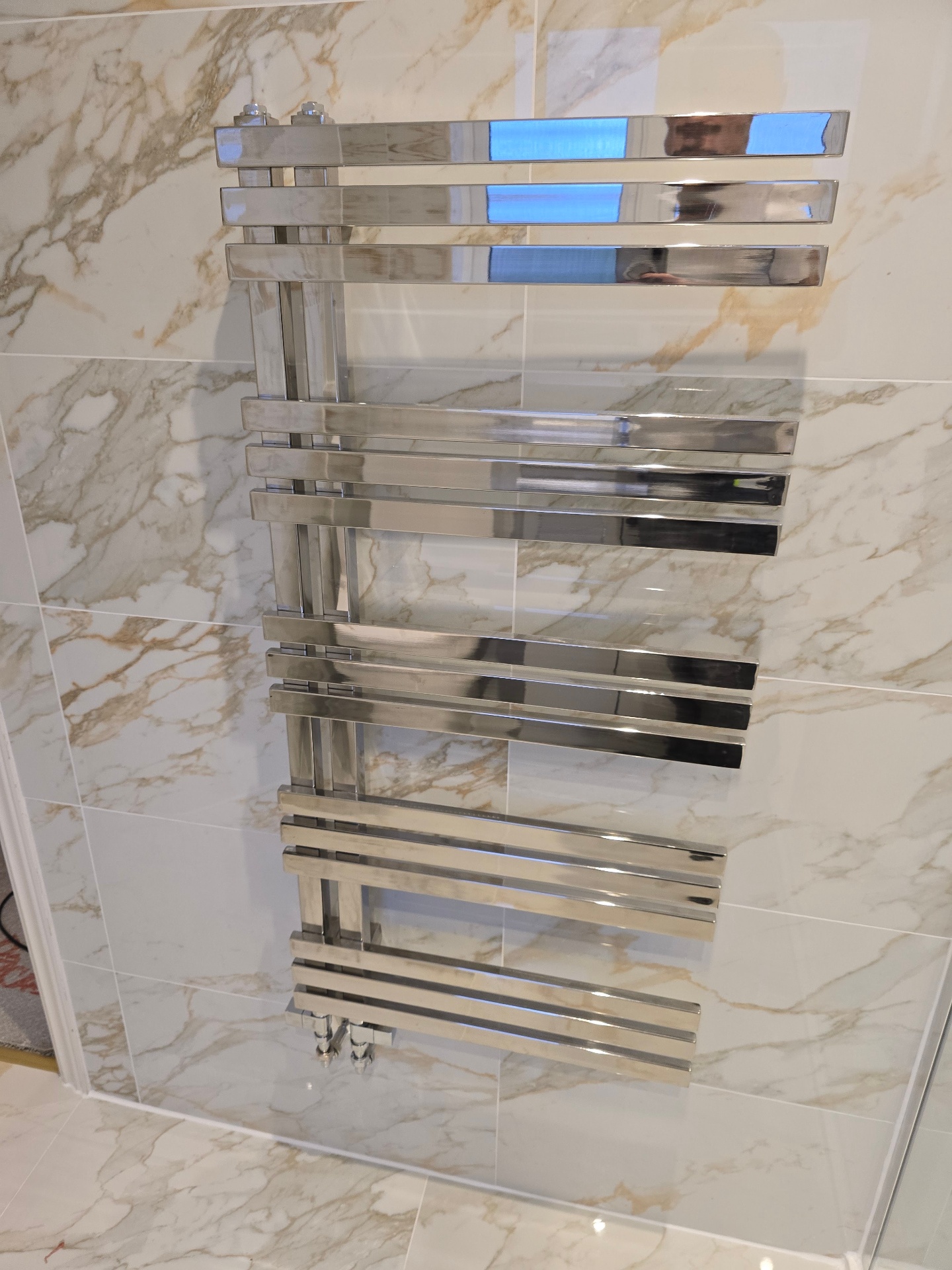 Designer chrome heated towel rail mounted on Calacatta marble-effect tiling in a luxury Tamworth bathroom